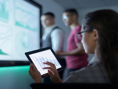 Una manager e due colleghi controllano dei dati su un grande schermo e su un tablet